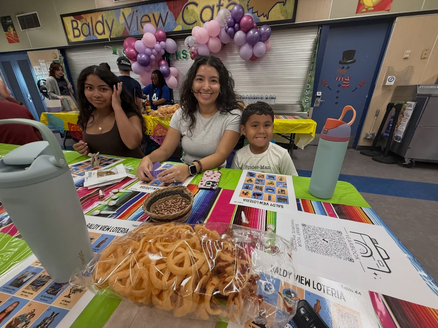 Baldy View family members and children gathered around a colorful Lotería table
