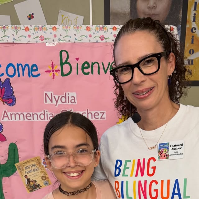 A Baldy View student and bilingual community guest smiling in front of a colorful Bienvenidos backdrop